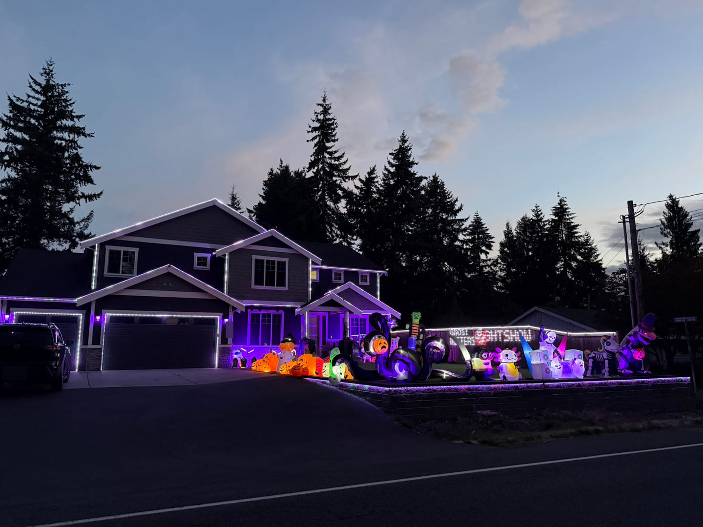 House With The Lights at dusk with purple lighting, orange pumpkins, Halloween characters, and a large tentacled creature across the front lawn